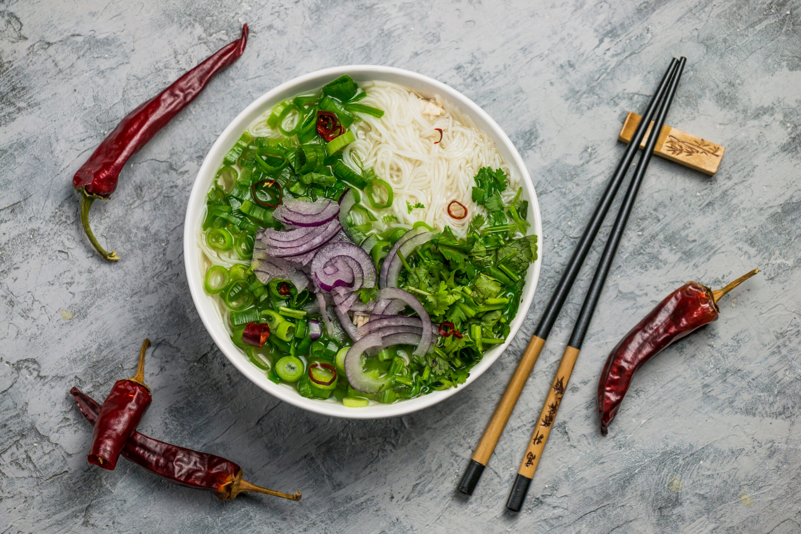 Served bowl of vietnamese soup pho ga with spring onion, chilli peppers and coriander on rustic background