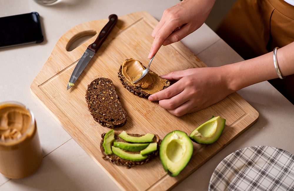 Woman making avocado peanut butter toast for a healthy breakfast at home