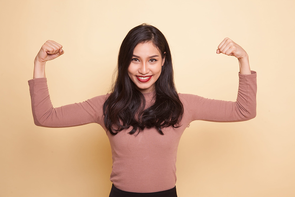 Beautiful young Asian woman flex bicep on beige background