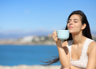 Cómo proteger tu piel del sol desde dentro Happy woman drinking coffee and smelling on the beach a sunny day