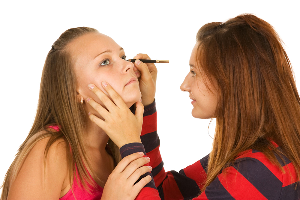 Two teenage girls dye their eyelashes isolated on white