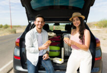 Si vas a comenzar tus vacaciones, esto te interesa Cheerful couple eating lunch in the car at the side of the road while making a long road trip together