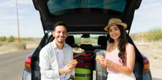 Si vas a comenzar tus vacaciones, esto te interesa Cheerful couple eating lunch in the car at the side of the road while making a long road trip together