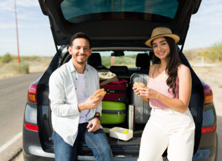 Si vas a comenzar tus vacaciones, esto te interesa Cheerful couple eating lunch in the car at the side of the road while making a long road trip together