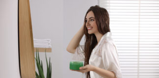 Mimos naturales para rehidratar la piel y el cabello Young woman applying aloe hair mask near mirror in bathroom