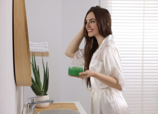 Mimos naturales para rehidratar la piel y el cabello Young woman applying aloe hair mask near mirror in bathroom